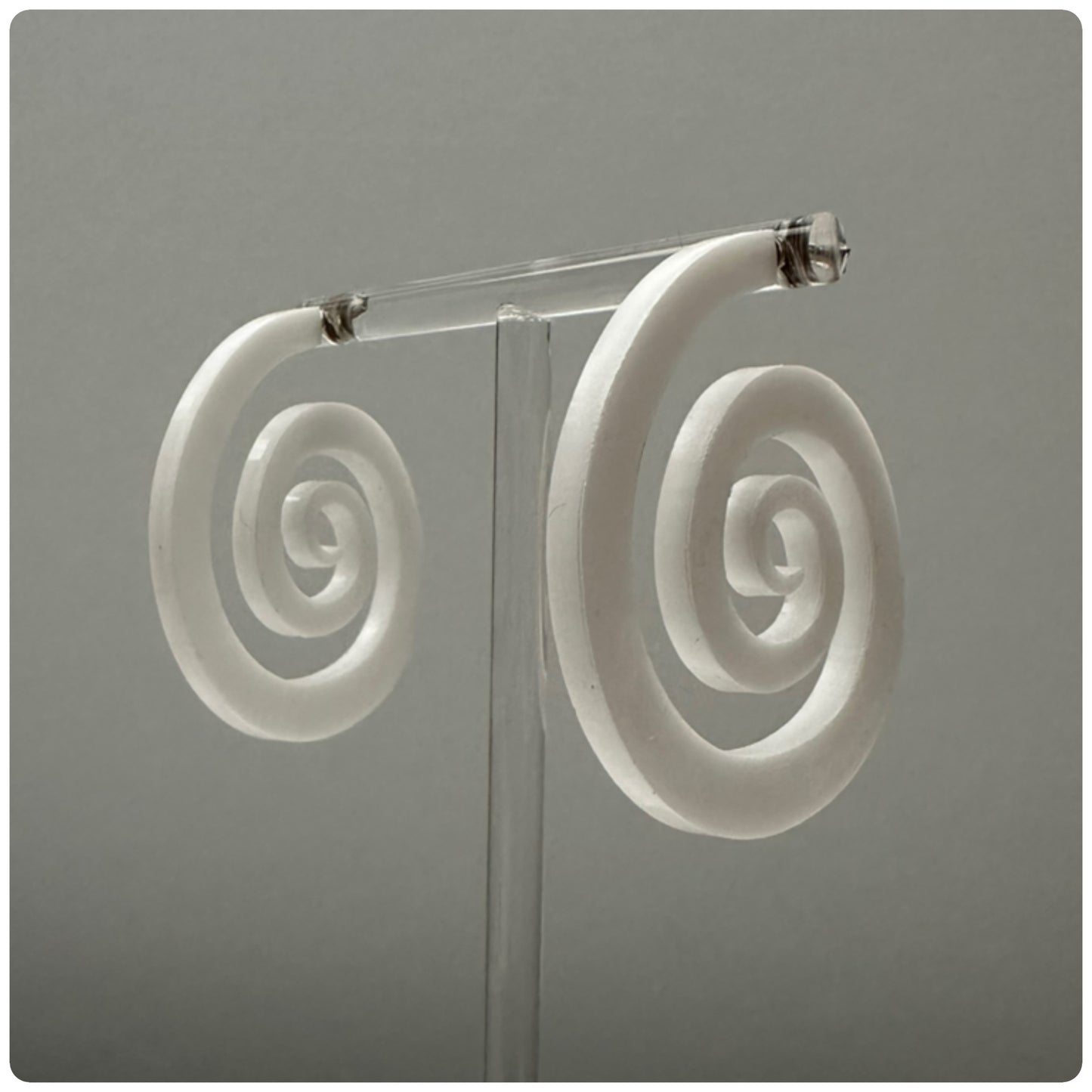 Striking lucite spiral hoop earrings. The spiral represents growth and evolution. The spiral’s outward movement signifies the idea of progress and forward motion. It encourages us to embrace change and continue growing, even when faced with challenges or obstacles. Meticulously handcrafted in the USA, these unique statement pieces feature sterling silver posts and are available in three stunning colors: Smokey grey, opaque white, and neon pink.